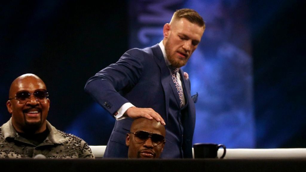 Conor McGregor places his hand over Floyd Mayweather's head