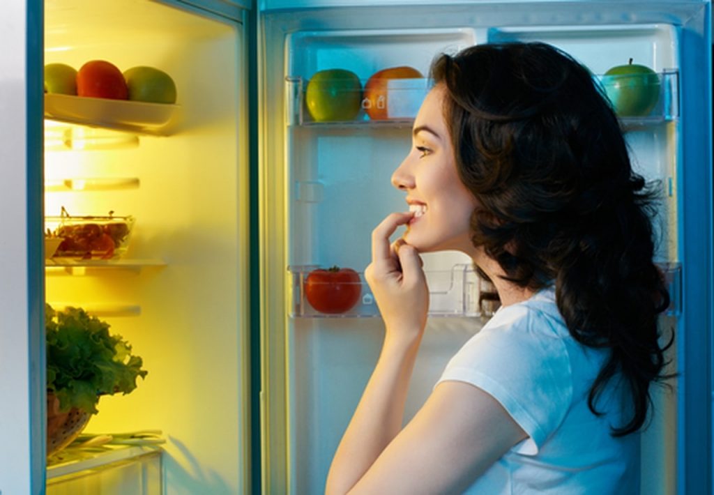 Woman looking inside a fridge white t shirt low calorie snacks