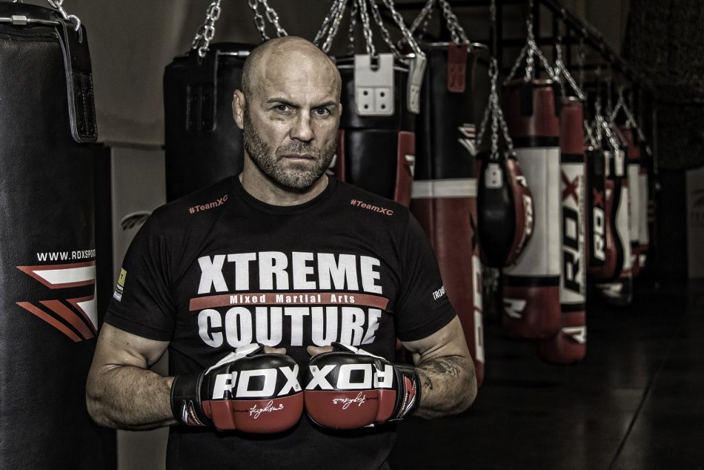 Randy Couture in black t shirt, red and black MMA glvoes inside a gym