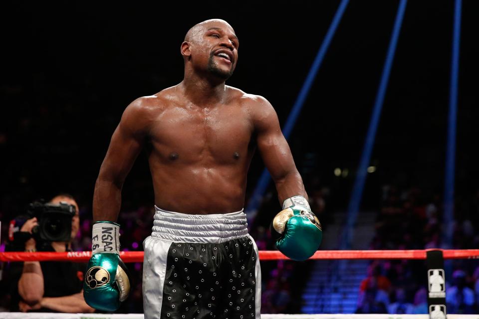 Floyd Mayweather smiles standing inside a boxing ring